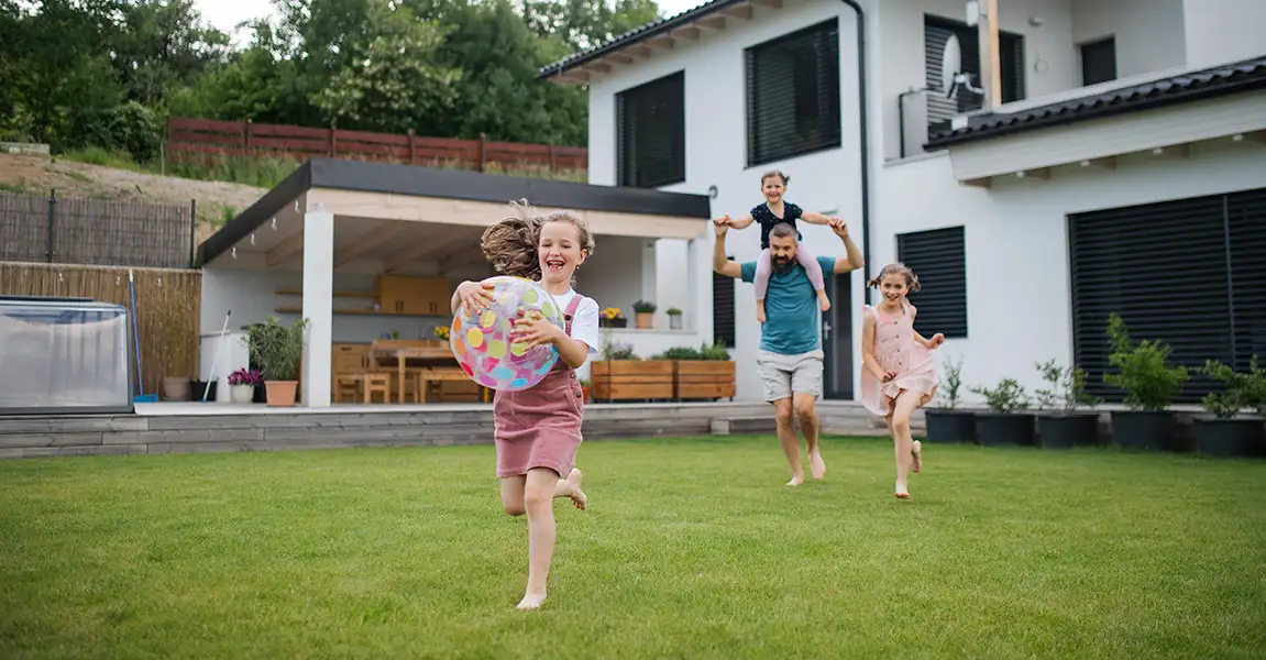 A happy family running and playing with a beach ball on a healthy, pest-free green lawn in their backyard.