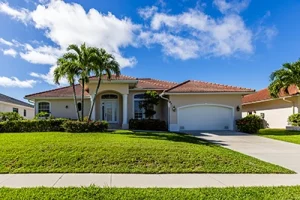 Front of a residential home in florida with palm trees and green grass