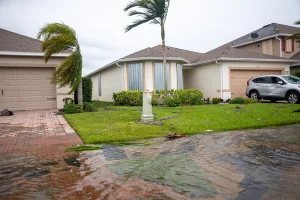A Florida home experiencing flood waters and high wind, blowing palm trees in front of the house.