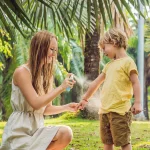 Mother applying mosquito repellent spray to her child outdoors