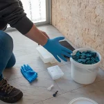 A pest control worker wearing gloves prepares bait stations and toxic blocks on a tile floor, showing practical steps for how to get rid of rats.